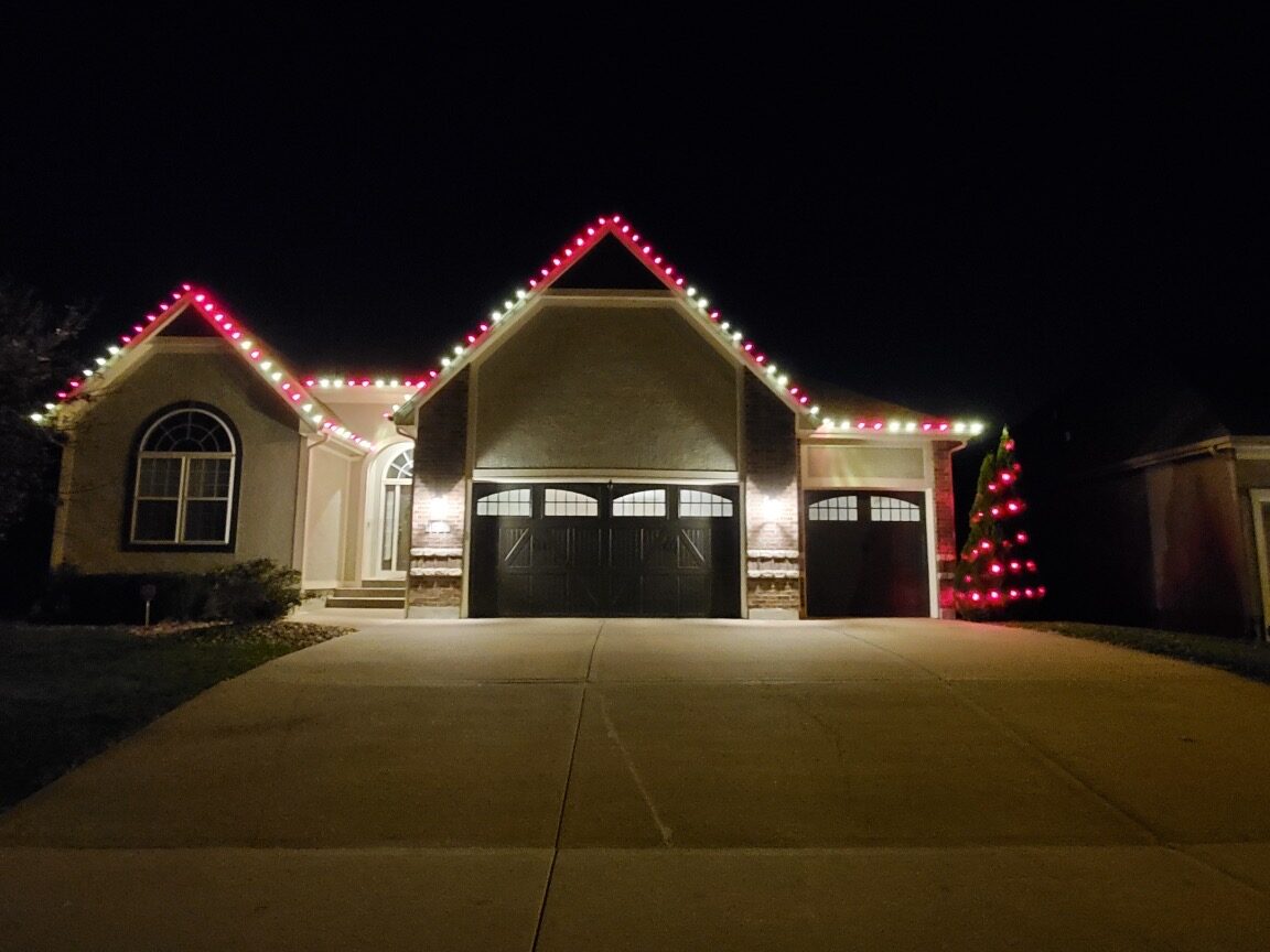 Red and white C9 lights with wrapped tree on three-car garage home